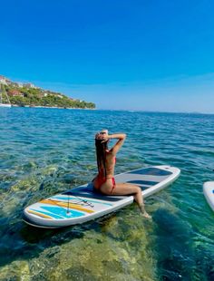 a woman sitting on top of a surfboard in the ocean next to another boat