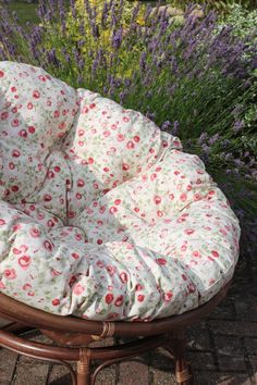 a round chair cushion sitting on top of a wooden table in front of purple flowers