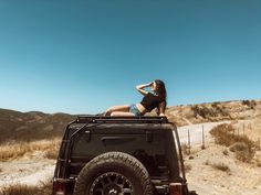 a woman sitting on the back of a black jeep with her hand in her hair