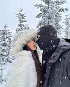 a man and woman are standing in the snow wearing winter clothes, one is covering his face with a hat