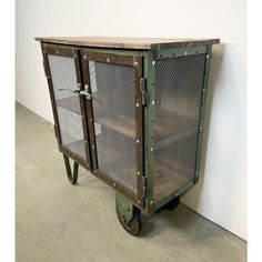 an old metal cabinet with mesh doors on it's sides and wheels, against a white wall