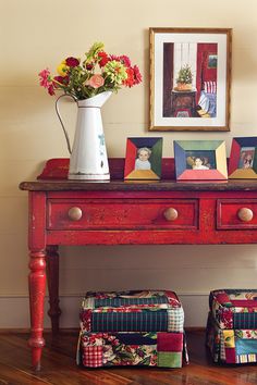 a red table topped with two vases filled with flowers next to pictures on the wall