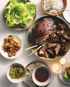 a table topped with plates and bowls filled with food next to candles, sauces and utensils