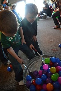 two young boys are playing with colorful balls in a metal bowl on the floor while others watch