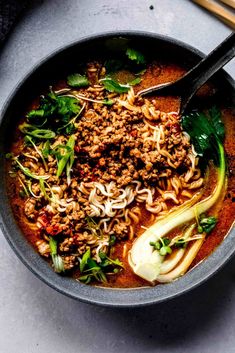 a bowl filled with meat and noodles next to chopsticks