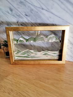 a wooden table topped with a glass frame filled with water and mountains covered in snow