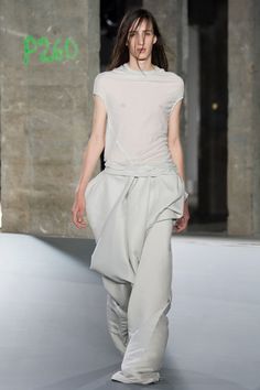 a woman walking down a runway wearing white pants and a short sleeved top with an asymmetrical design on it