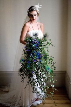 a woman in a wedding dress holding a bouquet with feathers on it's head