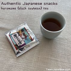 a cup of black tea next to a packet of japanese snacks on a white tablecloth