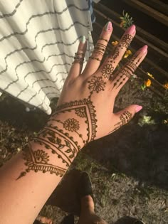 a woman's hand with henna tattoos on it and flowers in the background