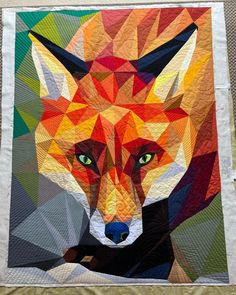 a close up of a quilt with a fox on it's face and green eyes