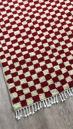 a red and white rug with fringes on the floor next to a wooden table