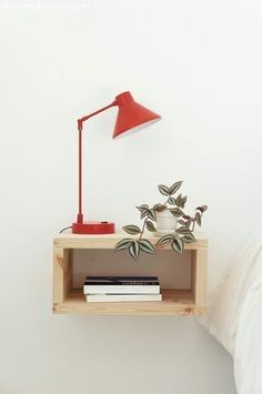 a red lamp on a wooden shelf next to a bed