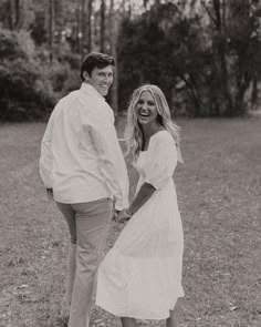 a man and woman holding hands while standing in the middle of a field with trees behind them