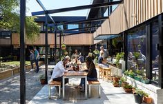 people are sitting at tables in an open courtyard with lots of plants and potted trees