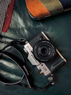 an old camera sitting on top of a green leather surface next to a wallet and cell phone