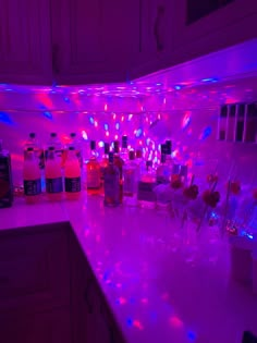 a kitchen counter topped with bottles and glasses filled with liquid next to lights on the wall