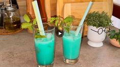 two glasses filled with blue liquid and green straws next to each other on a counter