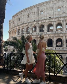 two women standing in front of the colossion looking at each other and talking