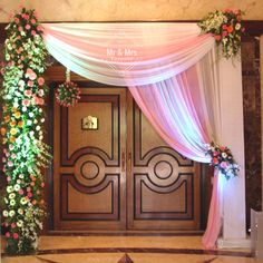 an entrance decorated with pink and white draping, flowers and greenery for a wedding