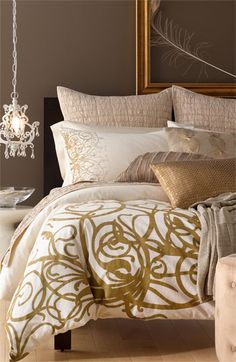 a bed with gold and white comforters in a bedroom next to a mirror on the wall