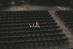 two people laying on the ground in an empty auditorium with rows of seats facing each other