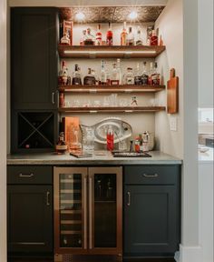 a kitchen with black cabinets and shelves filled with liquor bottles on top of the counter