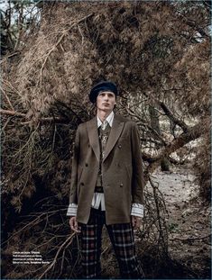 a man standing in front of a tree wearing a suit and tie with plaid pants