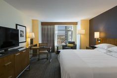 a hotel room with a large bed, desk and television in front of a window