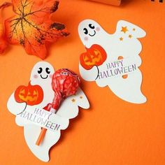 two halloween candy lollipops sitting on top of an orange table next to leaves