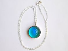 a necklace with a blue pendant hanging from it's side on a white surface