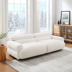 a white couch sitting on top of a wooden floor in front of two large windows