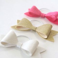 three little bows with gold, pink and white glitter on them sitting next to each other