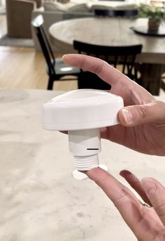 a hand holding a white object in front of a dining room table with black chairs