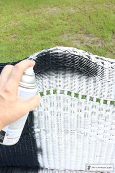 a person spray painting a wicker chair with white paint on the seat and green grass in the background