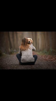 a woman sitting in the middle of a forest holding a dog on her head and looking up