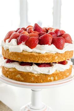 two layers of cake with strawberries on top and whipped cream around the edges, sitting on a white pedestal