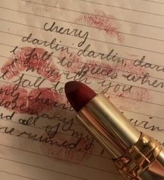 a close up of a lipstick on top of a piece of paper with writing in the background