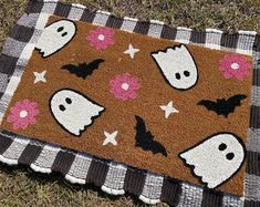 a halloween door mat on the ground with ghost and flowers around it, which is decorated in black and white checkered fabric