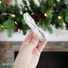 a hand holding a pair of scissors in front of a fireplace with christmas decorations on the mantle