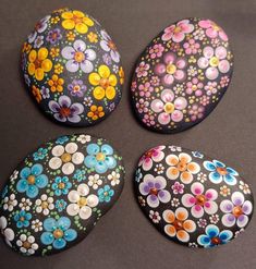 four painted rocks sitting on top of a black surface with different colors and sizes of flowers