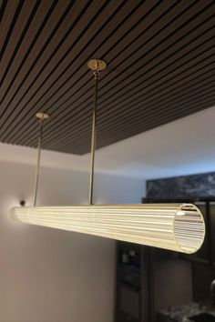 a modern light fixture hanging from the ceiling in a living room with wood slats on the ceiling