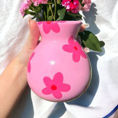 a hand holding a pink vase with flowers in it