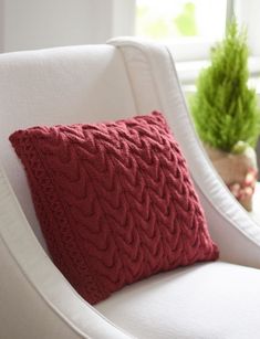 a red knitted pillow sitting on top of a white chair next to a mirror