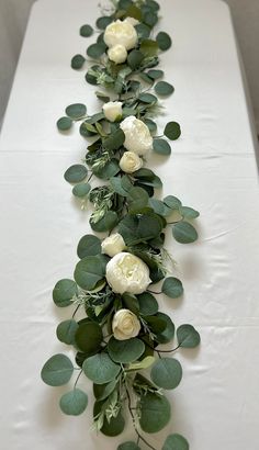 a long table with white flowers and greenery on it's sides, along with green leaves