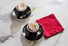 two cups of hot chocolate with whipped cream and gold spoons on a marble table