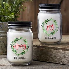 two jars with christmas candles on them sitting next to a potted plant in the background