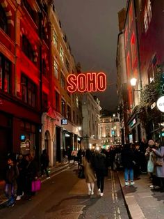 people are walking down the street in front of some buildings with neon signs above them