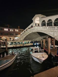 two boats are docked in the water under a bridge at night with people on it