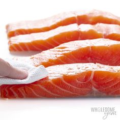 two pieces of raw salmon on a white surface with a person's hand holding the end